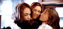 three women are hugging each other with one kissing the other on the cheek .