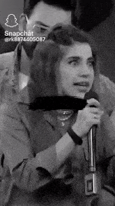 a woman is singing into a microphone while a man looks on .