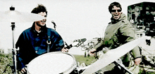 a man playing drums and another man playing a guitar in a band