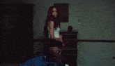 a woman with red hair is laying on a bed in a white tank top