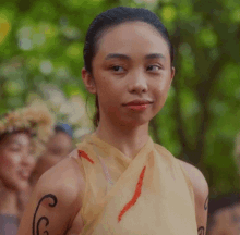 a woman with tattoos on her arms is standing in front of a group of people in a forest .