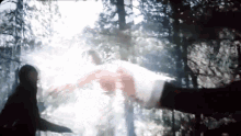 a person is standing in the woods with a sword in their hand and a person is flying through the air .