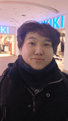 a young man stands in front of a store called kiki