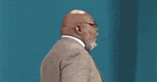 a bald man with a beard and glasses is wearing a suit and tie and making a funny face .