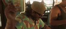 a man wearing a hat and sunglasses is sitting at a table with his arms outstretched .