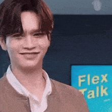 a young man is smiling in front of a blue sign that says flex talk .
