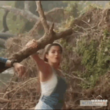 a woman in overalls is holding a tree branch in her hands .