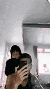 a man taking a picture of himself in a mirror with another man behind him