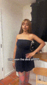 a woman in a black dress is standing in a kitchen with the words who won the diva off written below her .