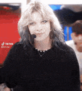 a woman with blonde hair and blue eyes is wearing a black shirt and a microphone on her head .