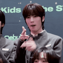 a young man in a suit and tie is pointing at the camera while standing in front of a sign that says kids .