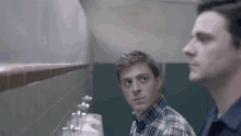 two men are standing next to each other in a public restroom looking at each other .