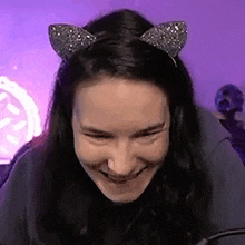 a woman wearing a cat ear headband is smiling while sitting in front of a microphone .