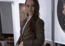 a woman in a suit and tie is standing in front of a wall with a painting on it