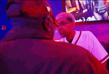 a man in a baseball uniform is talking to another man in a purple shirt .
