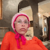 a woman wearing a pink hat and glasses is sitting in front of a mirror in a room .