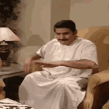 a man with a mustache is sitting in a chair and making a funny face .