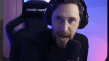 a man with a beard is wearing headphones and talking into a microphone while sitting in a chair .