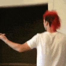 a man with red hair and a white shirt is standing in front of a black board .