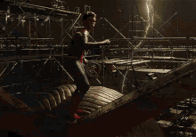 a man in a spiderman costume is standing on a ledge with a lightning bolt in the background