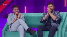 two men are sitting on a couch and clapping their hands with rtve written on the screen
