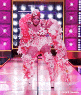 a drag queen is walking down a runway wearing a costume made of pink flowers .