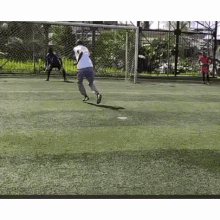 a man is kicking a soccer ball into a goal while a goalkeeper watches .