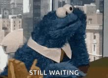 cookie monster from sesame street is sitting in front of a window with the words `` still waiting '' written on it .