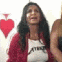 two women are standing next to each other in front of a red heart on a white wall .