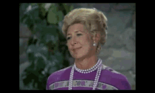 a woman wearing a purple shirt and pearls is smiling .