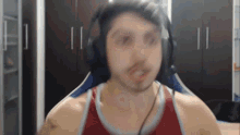 a man wearing headphones and a red tank top is looking at the camera .