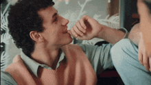 a man with curly hair wearing a pink sweater and a light blue shirt