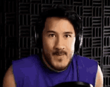 a man with a beard wearing headphones and a purple tank top is making a funny face .