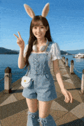a girl wearing bunny ears and overalls giving the peace sign
