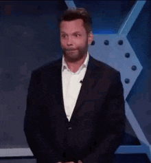 a man in a suit and white shirt is making a funny face while standing on a stage .