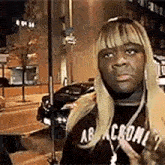 a man wearing a blonde wig and a black shirt is standing on a city street .