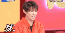 a man in a red shirt is making a funny face in front of a pink wall with chinese writing on it