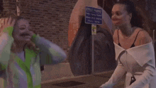a group of women are fighting in front of a restaurant with a neon sign that says ' tommy ' on it .