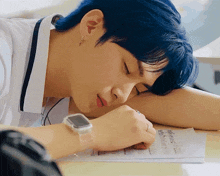 a boy with blue hair is laying down with his head on his arm and a watch on his wrist