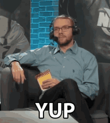a man wearing headphones is sitting in a chair holding a notepad and the word yup is on the table