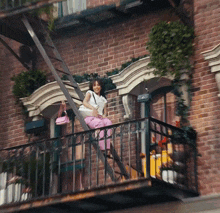 a woman sits on a fire escape on a brick building