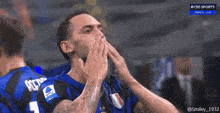 a man in a blue and black jersey with the number 1 on it is covering his mouth with his hands .