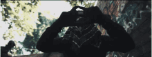a person making a heart shape with their hands in front of a wall with graffiti on it