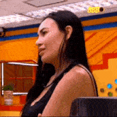 a woman with long black hair is standing in front of a yellow wall with a sign that says bbb on it .