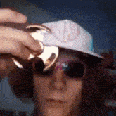 a man wearing a hat and sunglasses is holding a can in front of his face