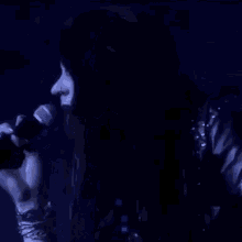 a woman is singing into a microphone on stage in a dark room .