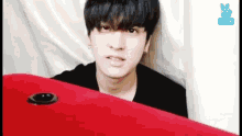 a young man is peeking out from behind a red table and making a funny face .