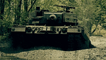a military tank is driving through a muddy field with trees in the background
