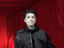 a man wearing a black jacket and a black scarf is standing in front of a red curtain