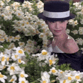 a woman wearing a black hat is standing in a field of flowers .